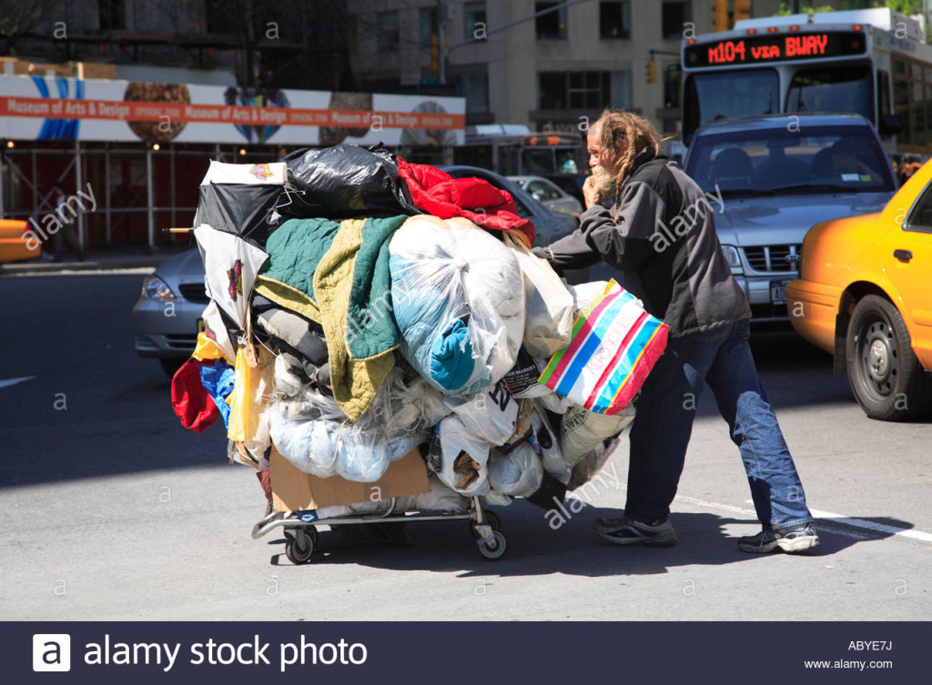 man-pushing-his-personal-belongings-in-a-shopping-cart-through-traffic-abye7j
